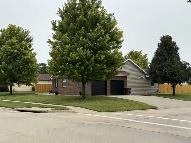 Brick and siding home features a two-car garage and mature trees.