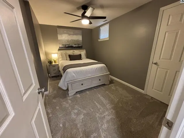 This bedroom features a ceiling fan, plush carpeting, and a neutral color palette.
