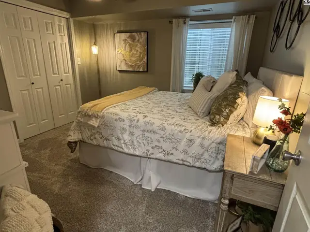 Carpeted bedroom with a queen-size bed, large closet, and a window with blinds.