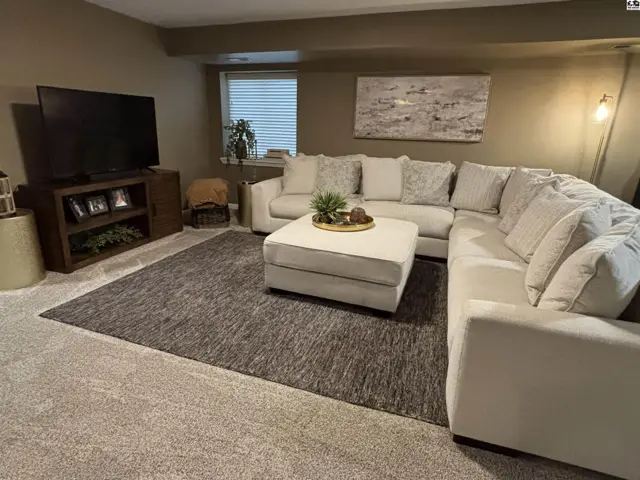Plush sectional sofa and ottoman anchor a carpeted living area with a large television.
