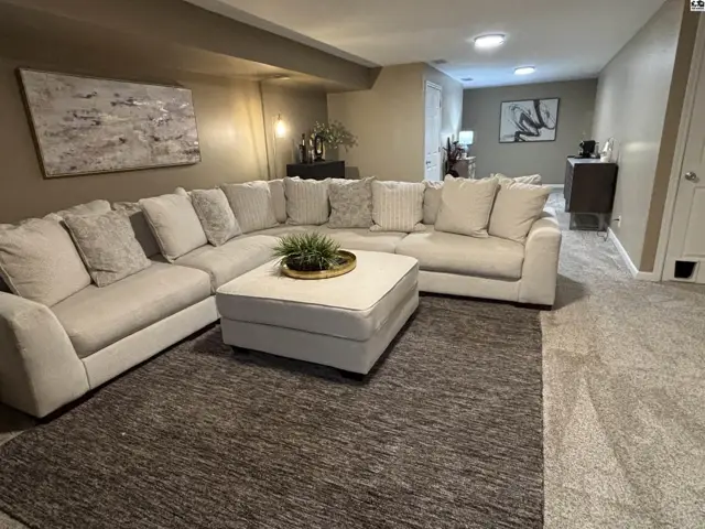 Spacious living area with a large sectional sofa, ottoman, and plush carpeting.