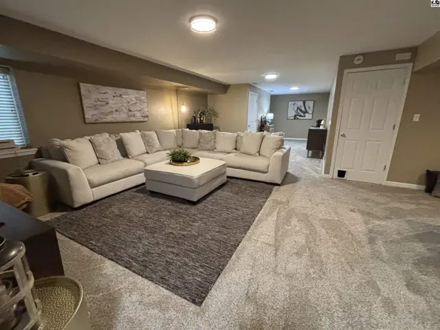 Spacious living area with plush carpeting, a large sectional sofa, and recessed lighting.