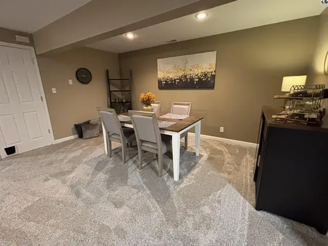 This room features a dining table, chairs, carpet, and a dark cabinet.