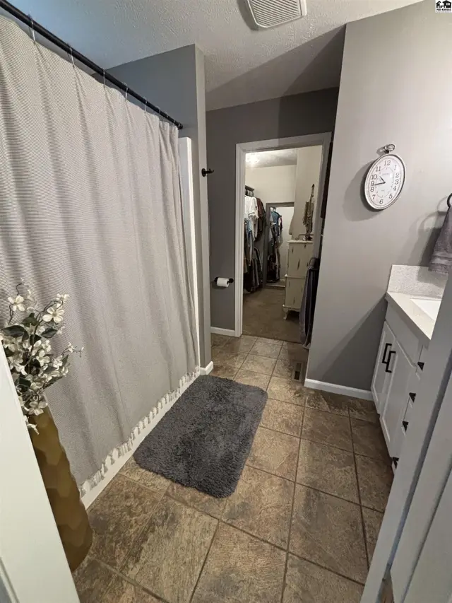 This bathroom features a tiled floor, white vanity, and a walk-in closet.