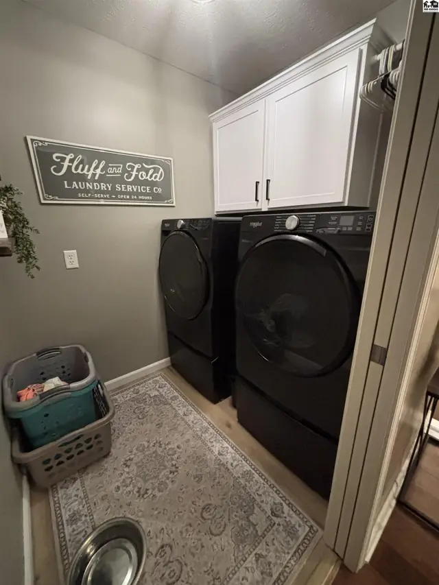 Laundry room with stacked black washer and dryer, white cabinetry, and a decorative sign.