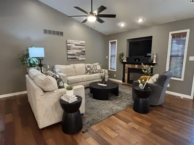 Vaulted ceiling living room features a fireplace, hardwood floors, and a ceiling fan.