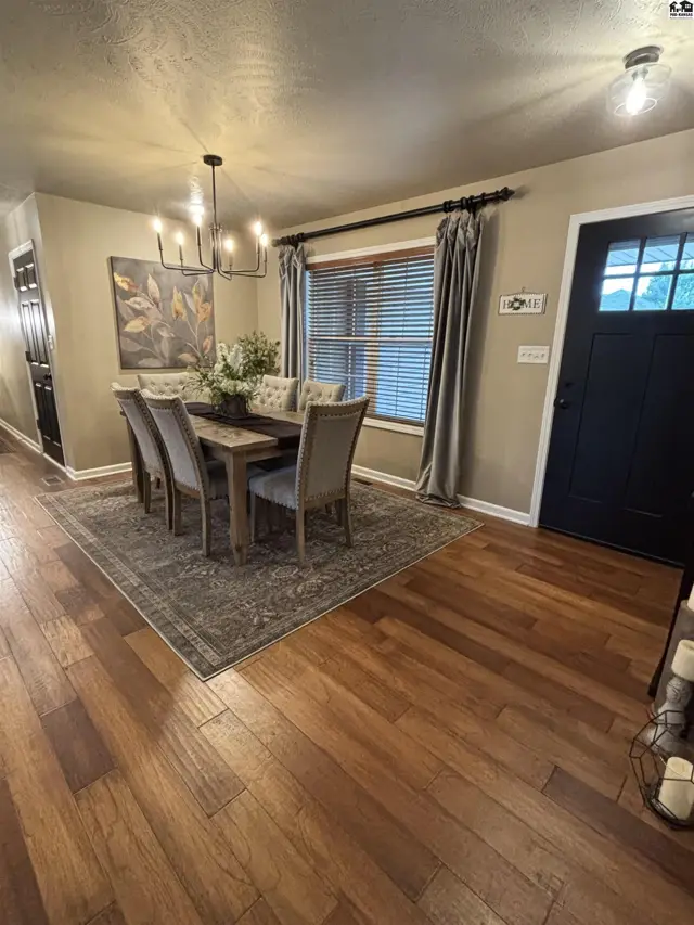 A dining room features a wood table, upholstered chairs, and a chandelier.