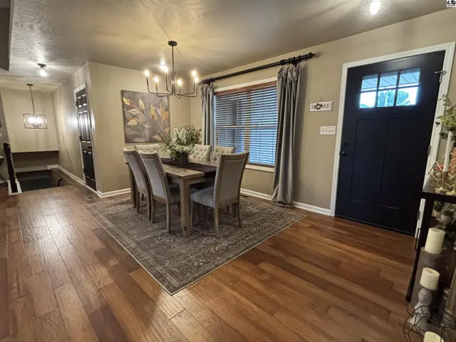 A dining room features a wood table, upholstered chairs, and a chandelier.