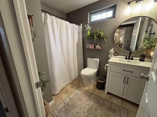 This bathroom features a white vanity, toilet, and shower with a white curtain.