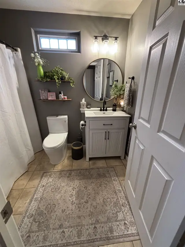 This bathroom features a vanity, toilet, shower with curtain, and tiled floor.