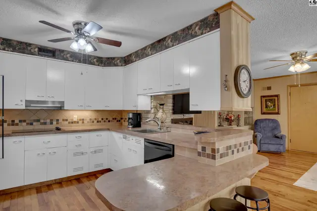 This kitchen features white cabinetry, a tiled backsplash, and a peninsula with seating.