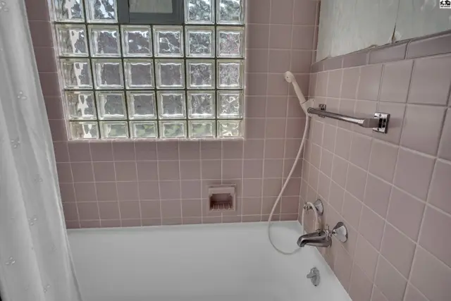 Bathtub with showerhead and tiled walls, featuring a glass block window.