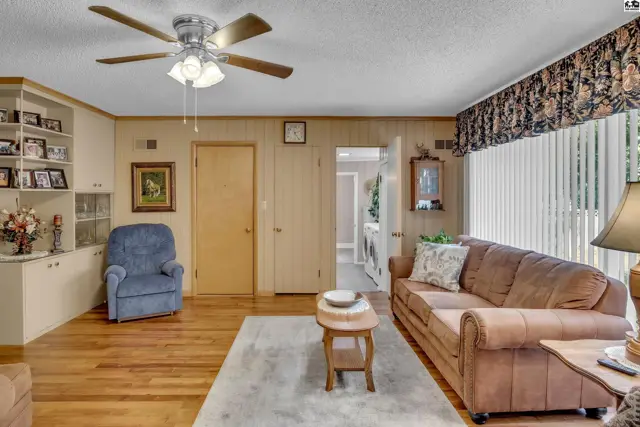 Spacious living room with wood-paneled walls, built-in shelving, and a ceiling fan.
