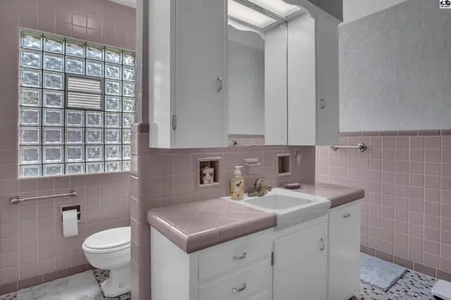 This bathroom features pink tile, a white vanity with a pink countertop, and a glass block window.