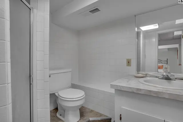 White tiled bathroom with a toilet, vanity, and glass-enclosed shower.
