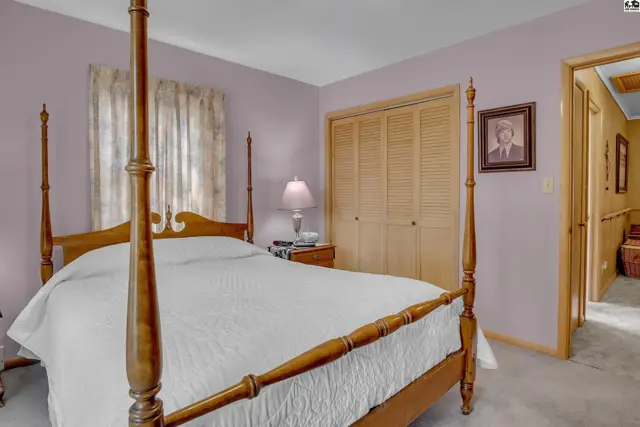 This bedroom features a wooden four-poster bed, a closet with louvered doors, and a framed portrait.