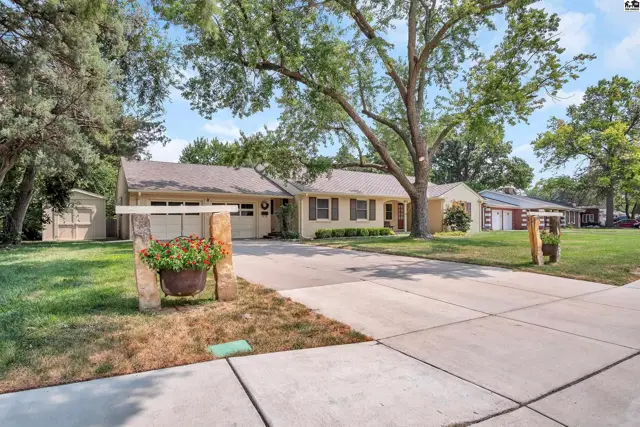 This single-story home features a light-colored exterior, attached garage, and mature trees.