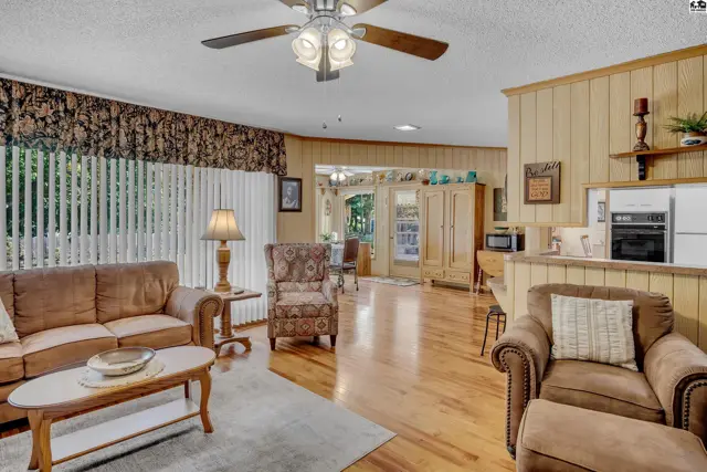 Spacious living area with wood-paneled walls, hardwood floors, and a ceiling fan.