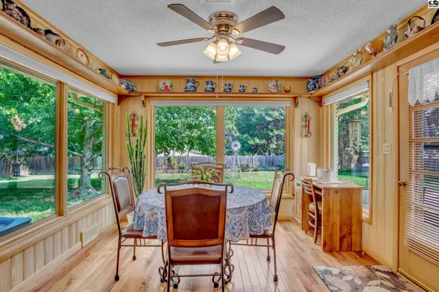 Sunlit dining area with large windows, wood paneling, and a ceiling fan.
