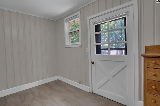 This room features paneled walls, a door with glass panes, and a wooden dresser.