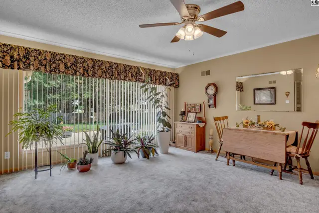 Carpeted room with large window, ceiling fan, and dining set.