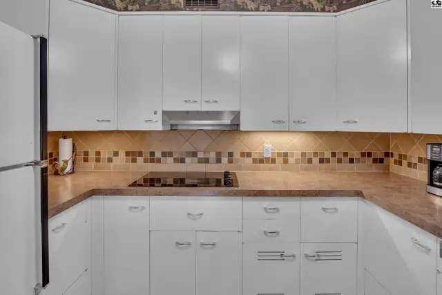 White cabinetry with a tiled backsplash and a built-in stovetop adorns this kitchen.
