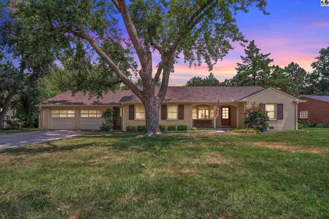 Brick ranch home with attached garage, mature trees, and manicured lawn.