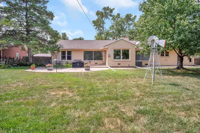 A light-colored stucco home with a patio and a decorative windmill sits on a grassy lawn.