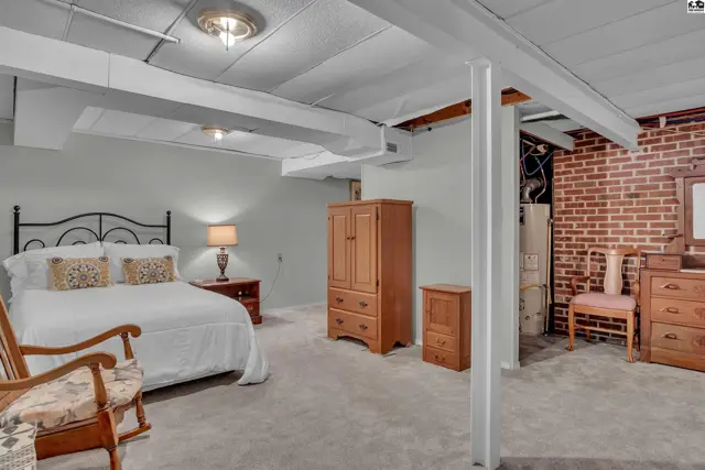 Spacious room with a bed, dresser, armoire, and exposed brick wall.