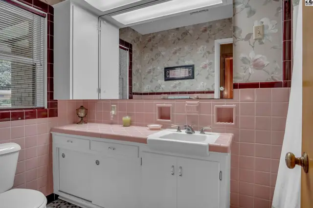 This bathroom features pink tile, a white vanity, and a large mirror.