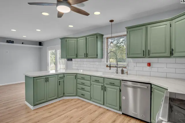 This kitchen features sage green cabinetry, white subway tile backsplash, and a stainless steel dishwasher.