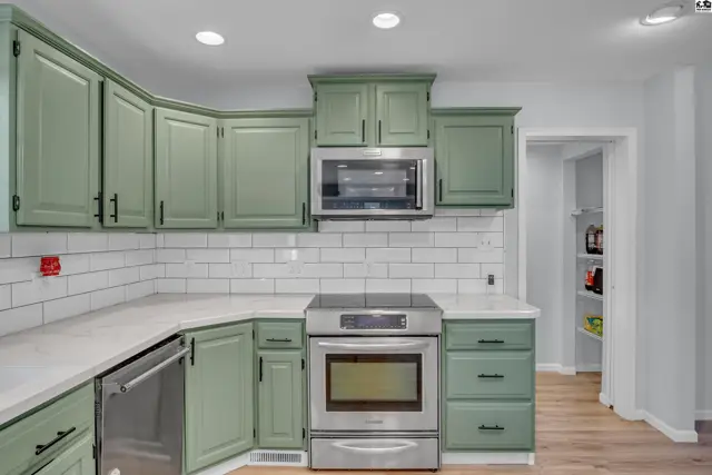 This kitchen features sage green cabinets, stainless steel appliances, and white subway tile backsplash.