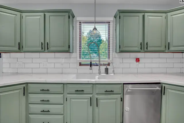 Sage green cabinets with black hardware complement white subway tile and quartz countertops.