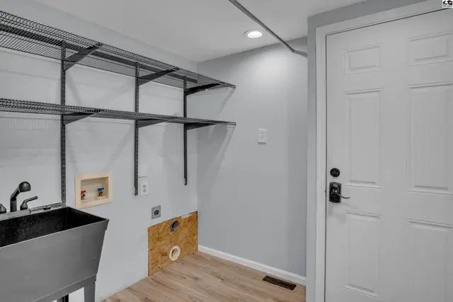 This laundry room features a utility sink, shelving, and a white door.