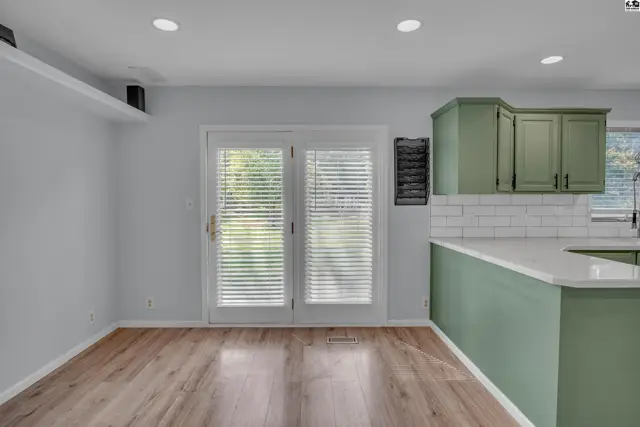 This kitchen features green cabinetry, white subway tile backsplash, and a large island with a white countertop.