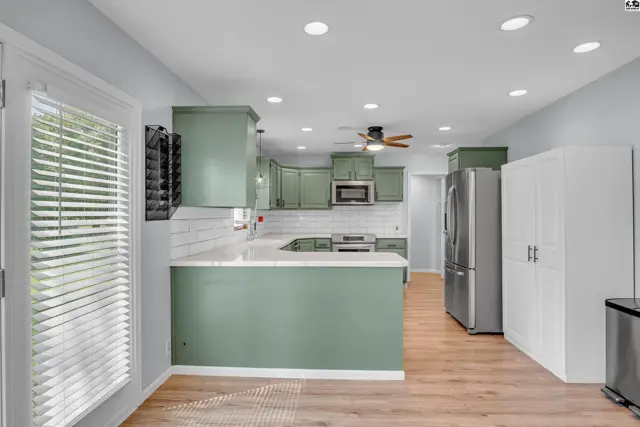 Spacious kitchen features sage green cabinetry, white subway tile backsplash, and stainless steel appliances.