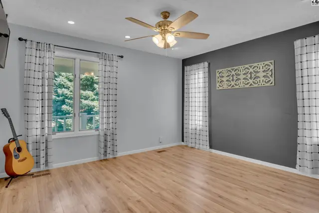 Light-filled room with wood-look flooring, a ceiling fan, and large windows.