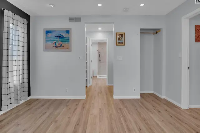 This room features light wood-look flooring, white walls, and a large window with a patterned curtain.