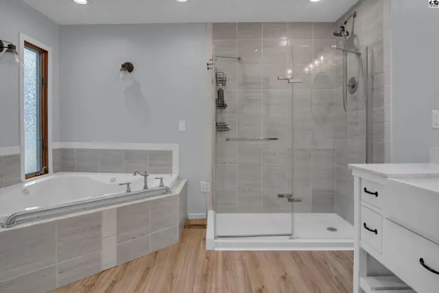 Spacious bathroom features a soaking tub, glass-enclosed shower, and double vanity.