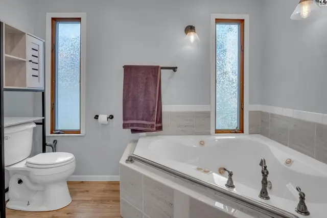 Spacious bathroom features a large corner tub, toilet, and storage shelves.