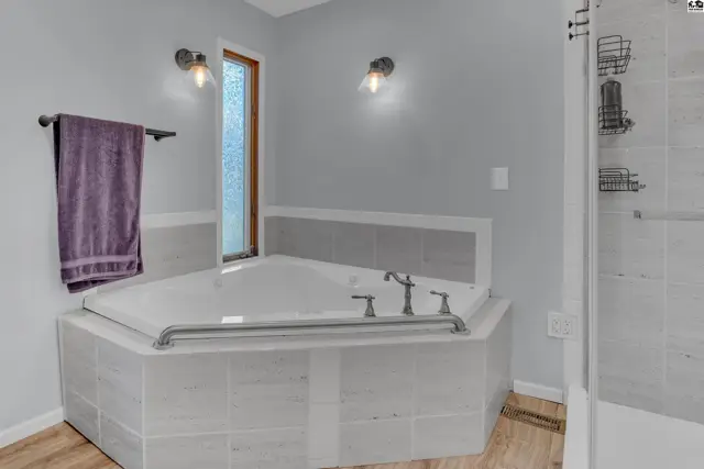 Spacious bathroom features a large corner soaking tub with tiled surround and a separate shower.