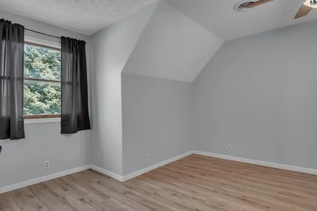 Light-filled room with sloped ceiling, wood-look flooring, and dark curtains.