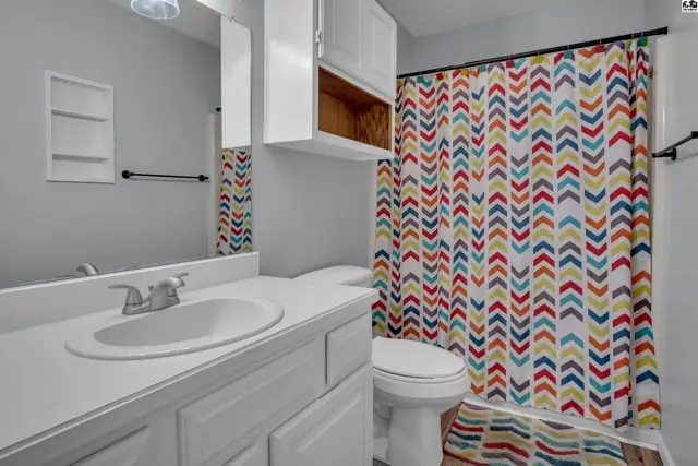 This bathroom features a white vanity, toilet, and a colorful chevron shower curtain.