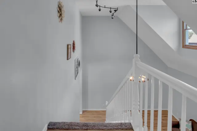 A white railing lines a staircase with wood flooring and light gray walls.