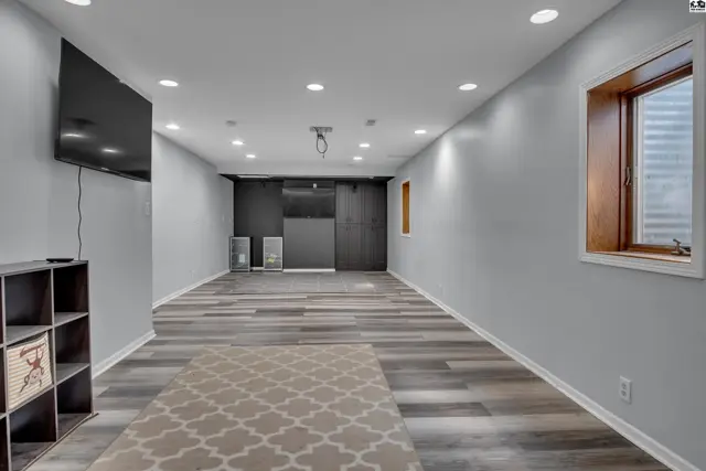Finished basement with grey wood-look flooring, recessed lighting, and a mounted television.