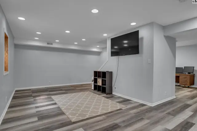Spacious finished basement with recessed lighting, wood-look flooring, and a mounted television.