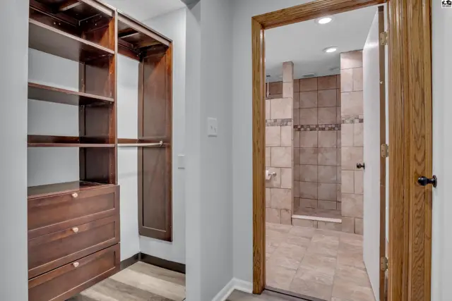 Spacious walk-in closet with built-in shelving and drawers opens to a tiled shower room.