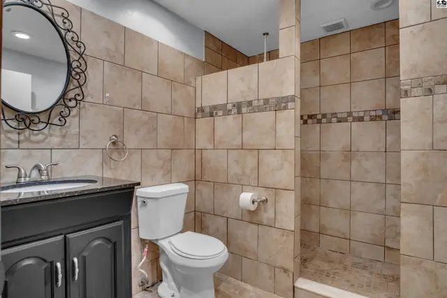 This bathroom features a vanity with a granite countertop, a tiled shower, and a toilet.