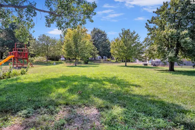 Spacious green lawn with mature trees and a playground structure.