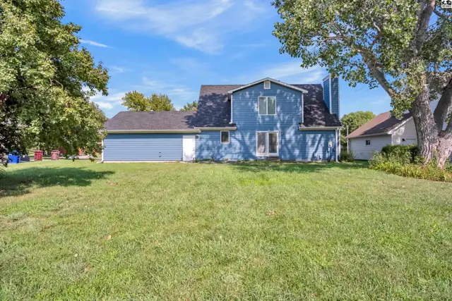 Blue siding house with a large green lawn and mature trees.